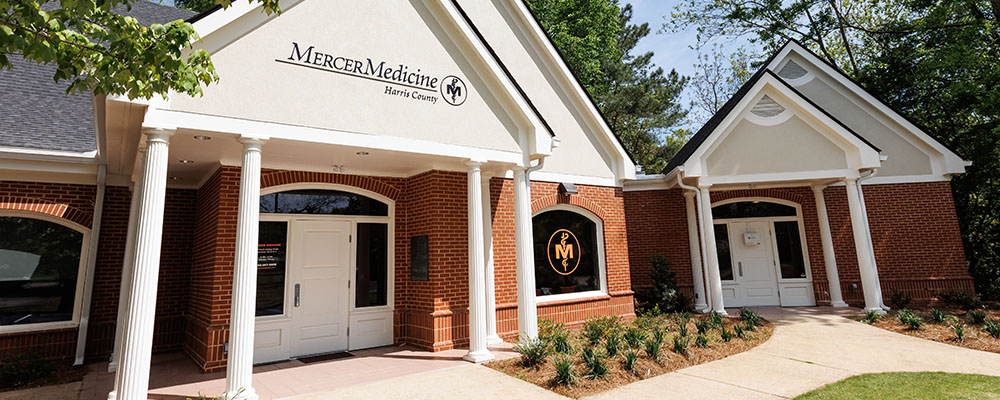 A red brick building with triangle arched roofs. A mercer medcine logo can be seen on a window. to the right of the door.